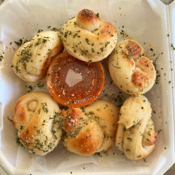 Garlic knots from Town Center Pizzeria, sprinkled with herbs and parmesan, with a side of marinara sauce.