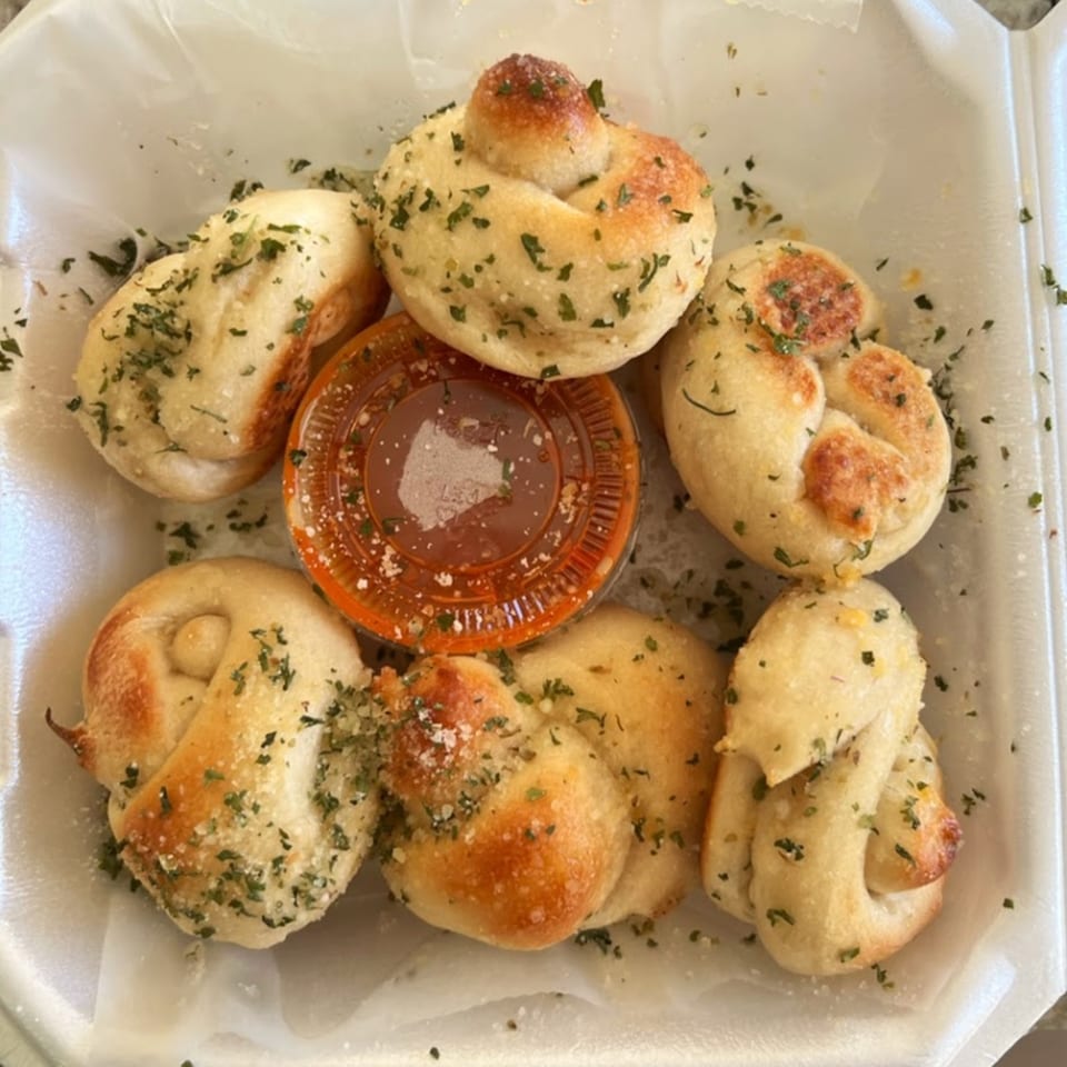 Garlic knots from Town Center Pizzeria, sprinkled with herbs and parmesan, with a side of marinara sauce.