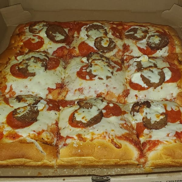 Close-up of a rectangular Town Center Pizzeria pizza with pepperoni, sausage, and melted cheese.