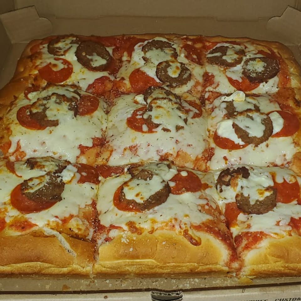 Close-up of a rectangular Town Center Pizzeria pizza with pepperoni, sausage, and melted cheese.