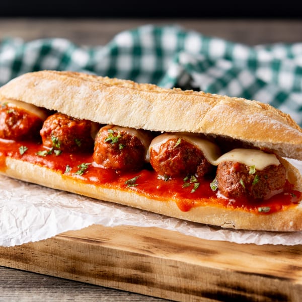 Meatball sub with melted cheese and red sauce on a wooden board with a green checkered napkin.