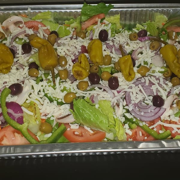 A large catering tray of fresh salad with lettuce, tomatoes, onions, olives, peppers, and cheese.
