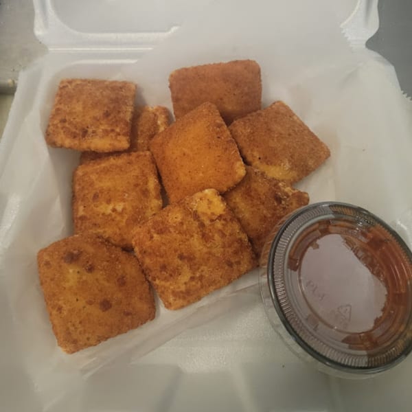 Golden-brown toasted ravioli with a side of marinara sauce in a white takeout container.