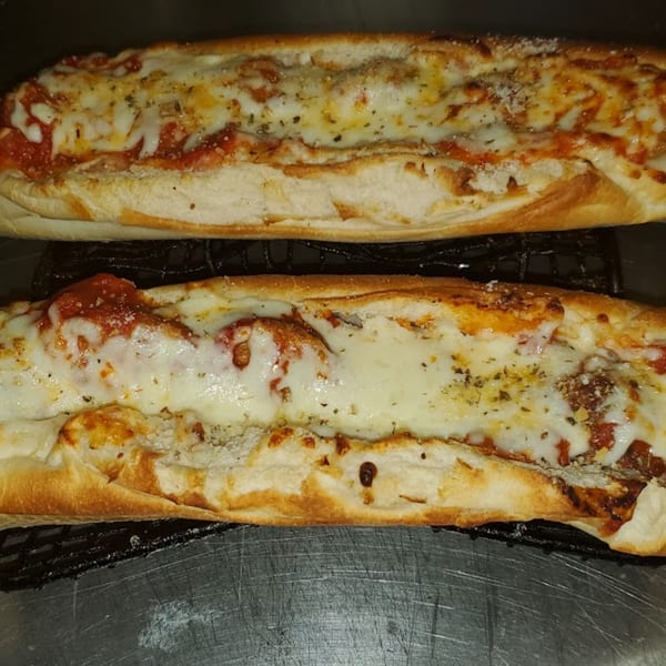 Two cheesy meatball subs with marinara sauce and herbs on a metal surface.